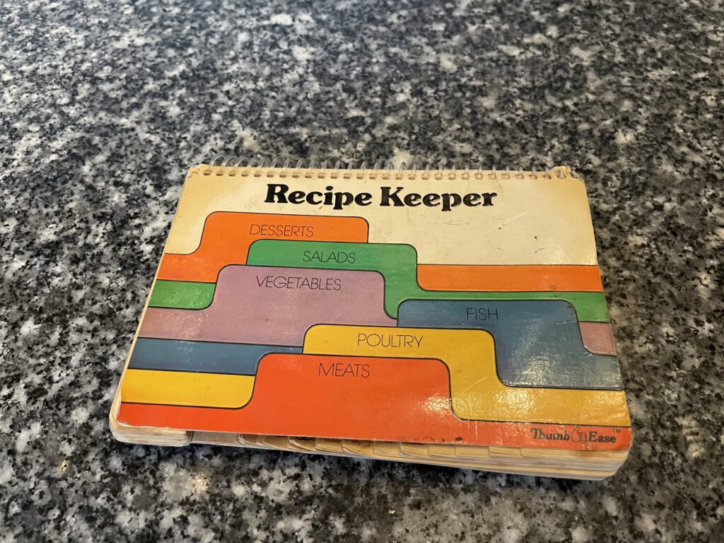 a multi-colored, spiral bound recipe keeper. There are tabs across the bottom of these landscape oriented cards that flip along the long edge at the top.